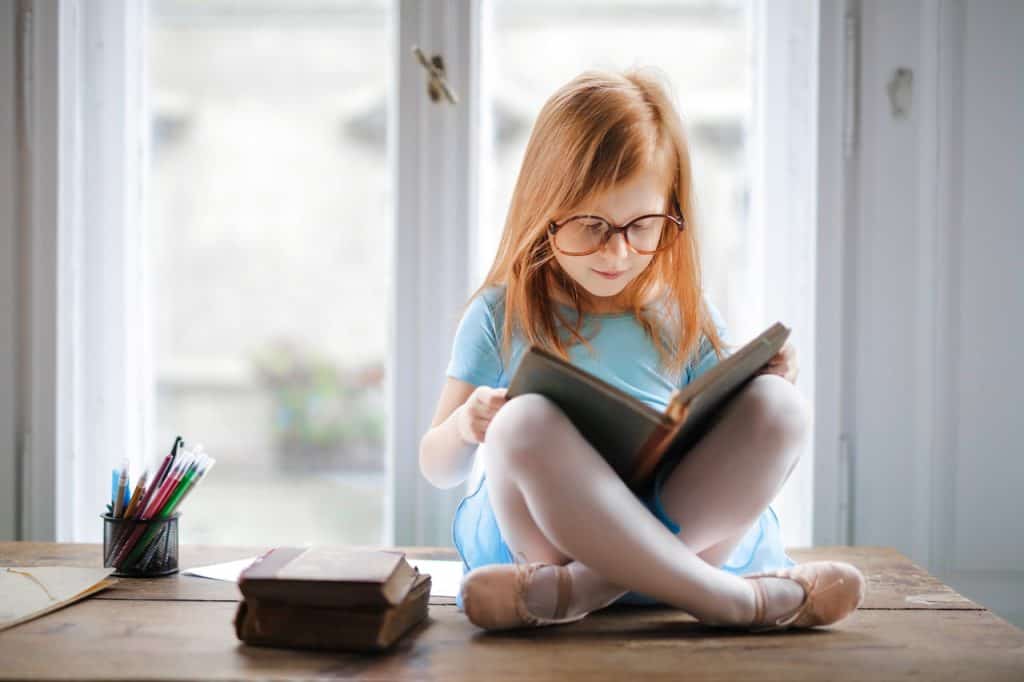girl with red hair reading in window